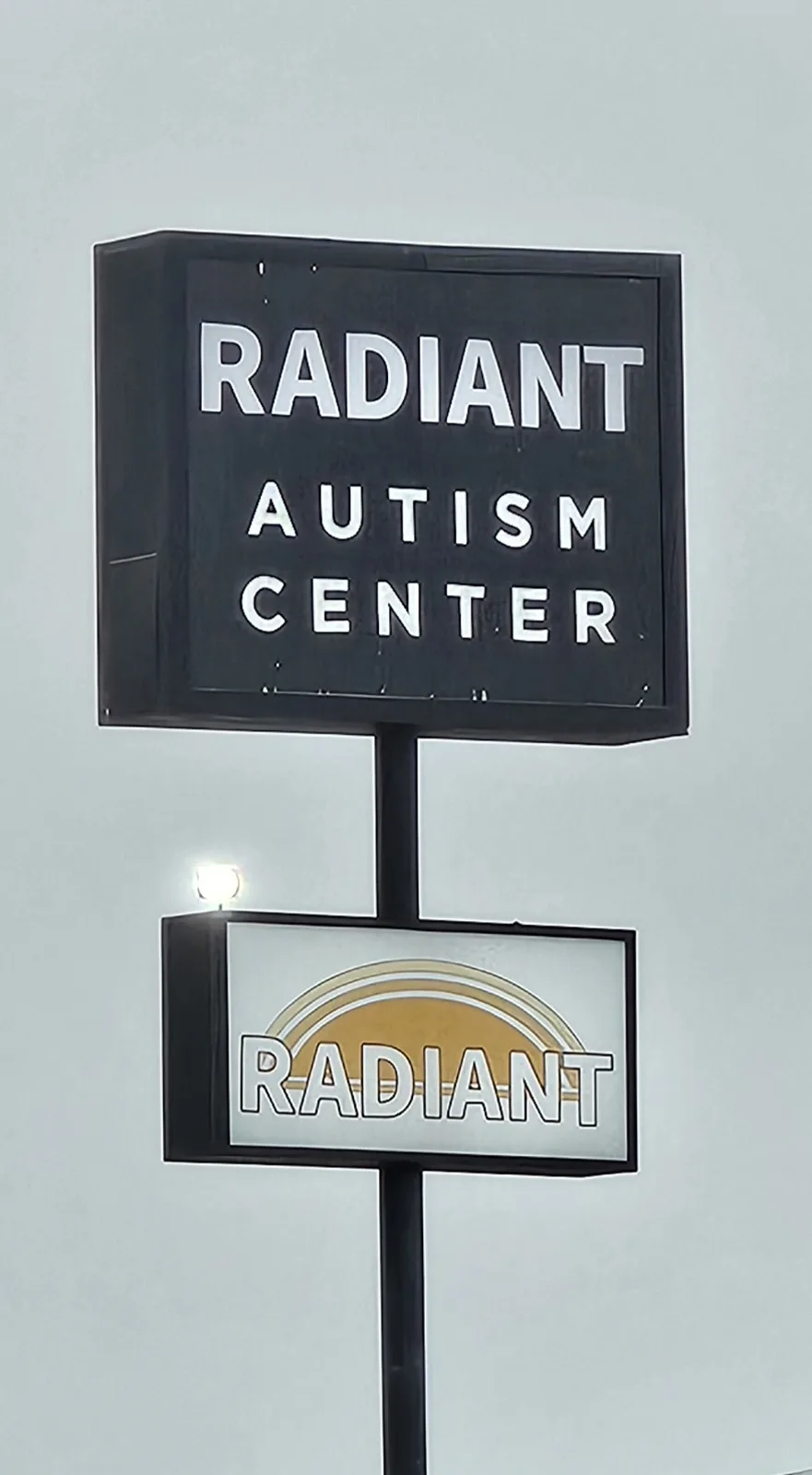 A black sign reads 'RADIANT AUTISM CENTER' in white letters, mounted above a smaller sign with 'RADIANT' and a sunburst…