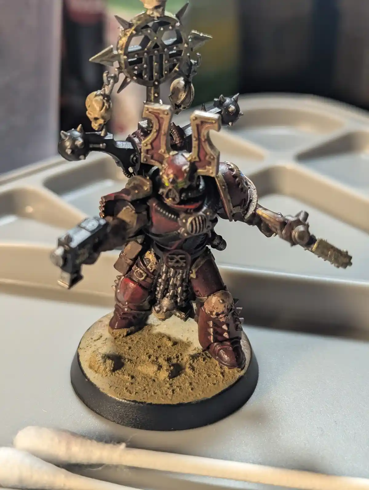 A heavily detailed, custom-painted miniature of a Warhammer 40,000 Chaos Space Marine stands on a textured base, holding a…