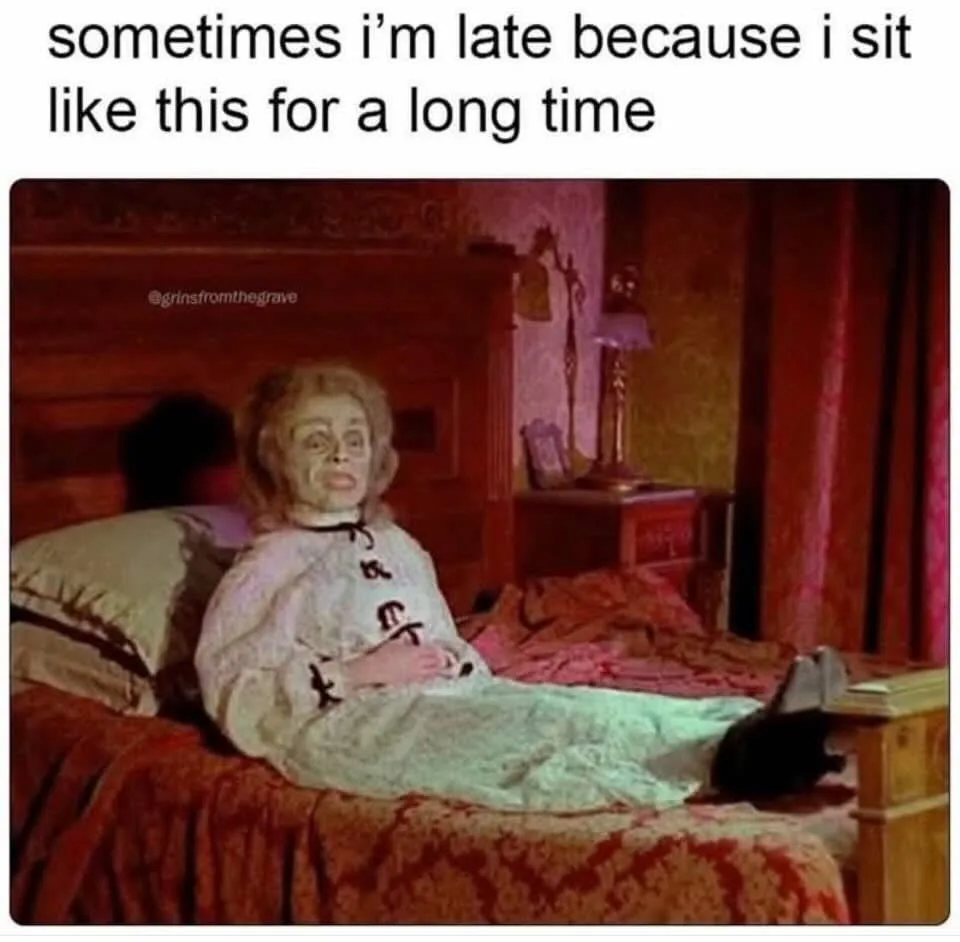 A person with a pale, gaunt face and blonde hair sits propped up in bed, wearing a white nightgown with black markings…