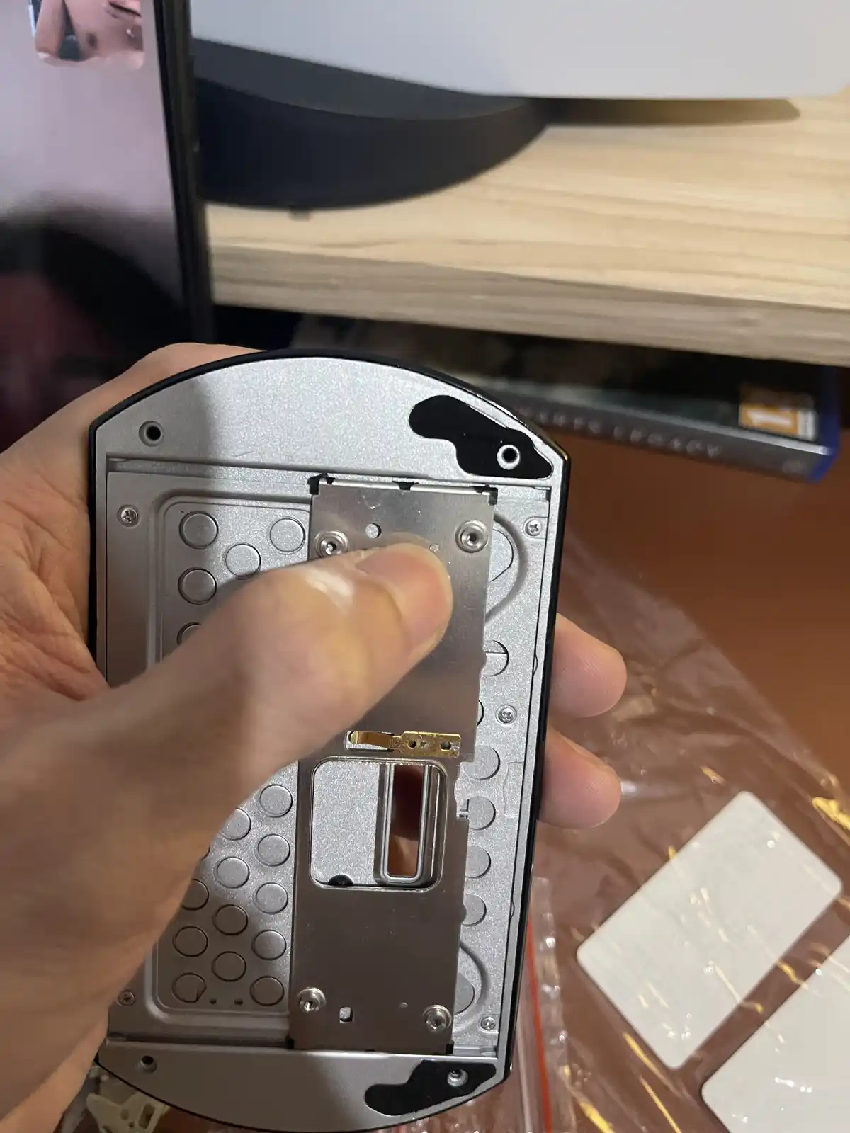 A hand holds the back of a disassembled silver phone, revealing its internal metal frame, screws, and circuitry. A finger…