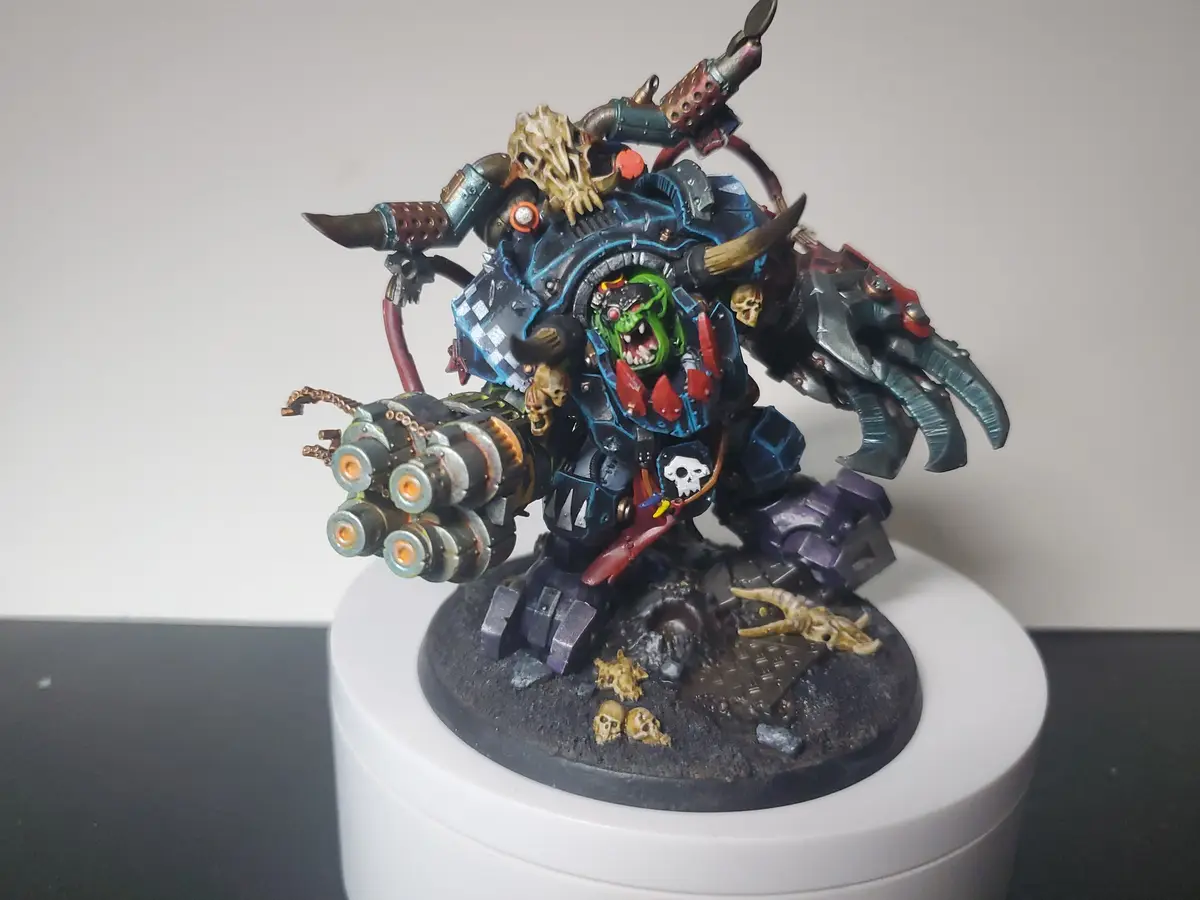 A heavily detailed, painted miniature of a green-skinned, horned, armored orc-like warrior with multiple weapons and skulls…