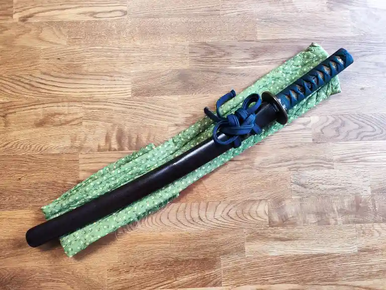 A black, blunt, stick-like object with a blue-wrapped handle and a decorative blue knot rests on a green patterned fabric…