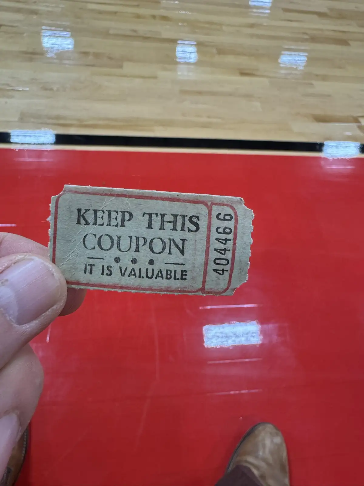 A hand holds a small, torn paper coupon with the text 'KEEP THIS COUPON IT IS VALUABLE' and the number '404466' printed on…