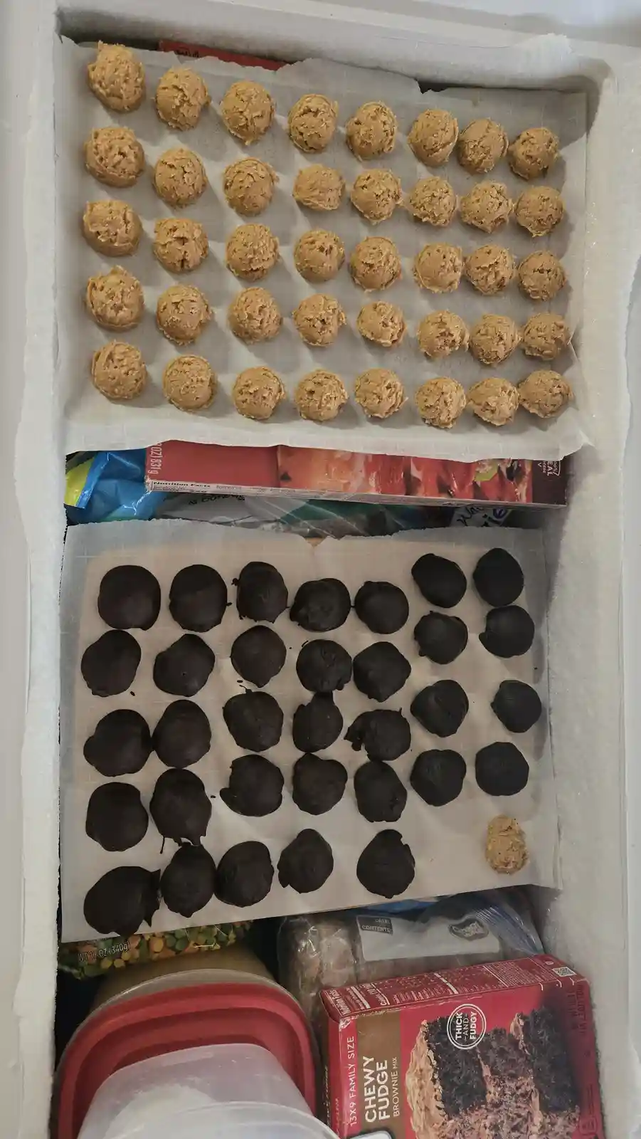 An overhead photo shows two trays of cookie dough balls inside a freezer. The top tray holds neatly arranged, undipped…