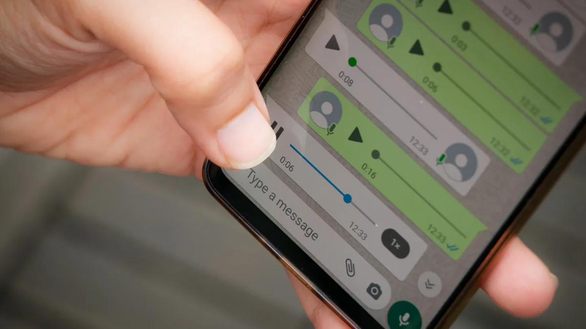 A close-up of a person's thumb hovering over a smartphone screen displaying a messaging app with voice messages. The screen…
