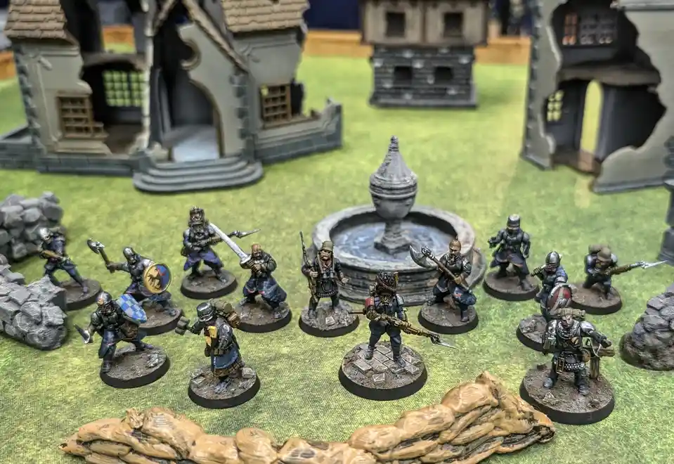A photo of numerous painted miniature fantasy soldiers in medieval-style armor, wielding swords, axes, and shields, arranged…