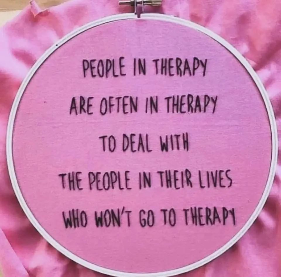 A pink fabric stretched in a white embroidery hoop displays black handwritten text that reads: 'PEOPLE IN THERAPY ARE OFTEN…