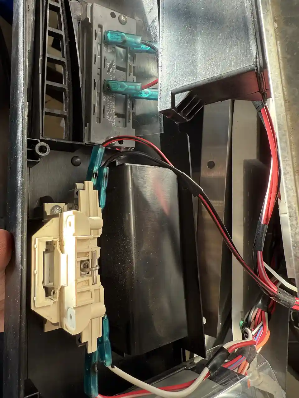 A close-up photo shows the internal wiring and components of an appliance, with a hand holding a beige plastic switch…