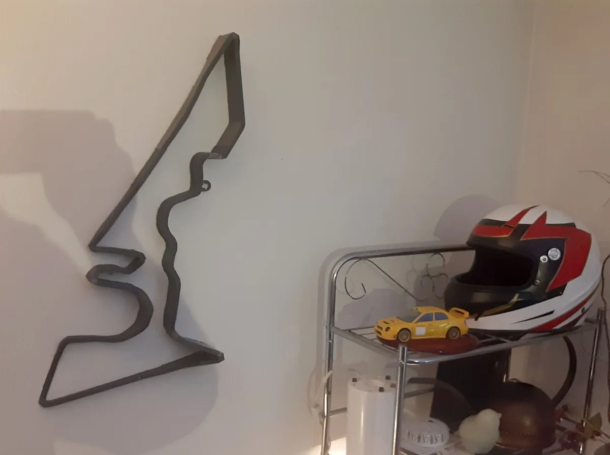 A metal track layout decoration is mounted on a white wall, next to a metal shelf holding a racing helmet and a yellow toy…