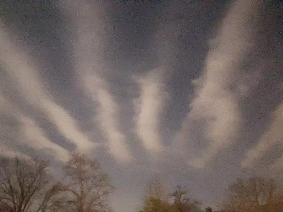 A low-resolution photo shows a cloudy sky with dark grey clouds and lighter, wispy cloud formations that resemble a ghostly…