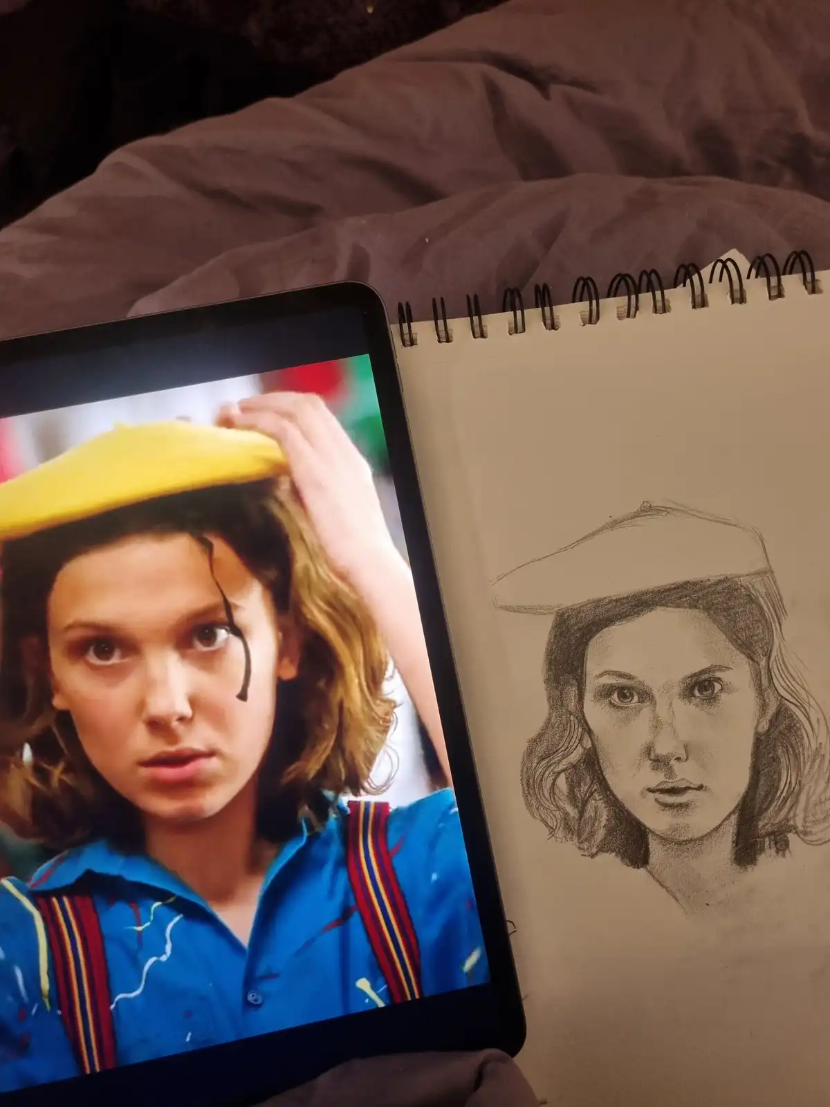 A tablet displays a colorful photo of a young woman with a yellow beret and paint-splattered blue shirt, next to a…