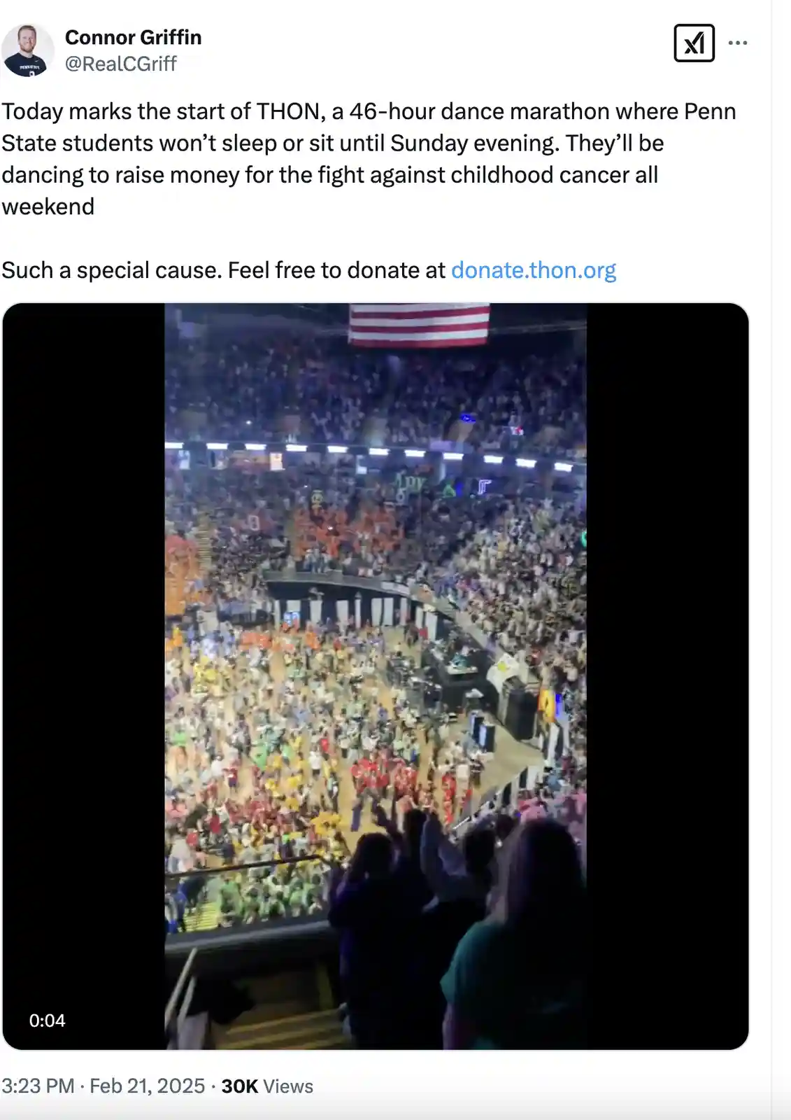 An overhead view of a massive indoor arena packed with thousands of people dancing in colorful groups, with an American flag…
