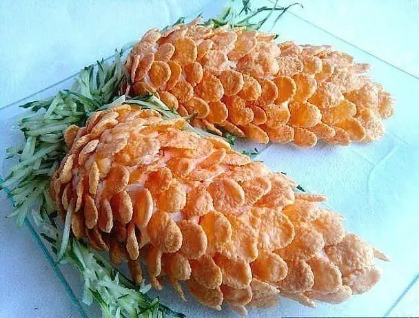 Two pinecone-shaped food sculptures made entirely of orange cornflakes are arranged on a clear glass plate, surrounded by…
