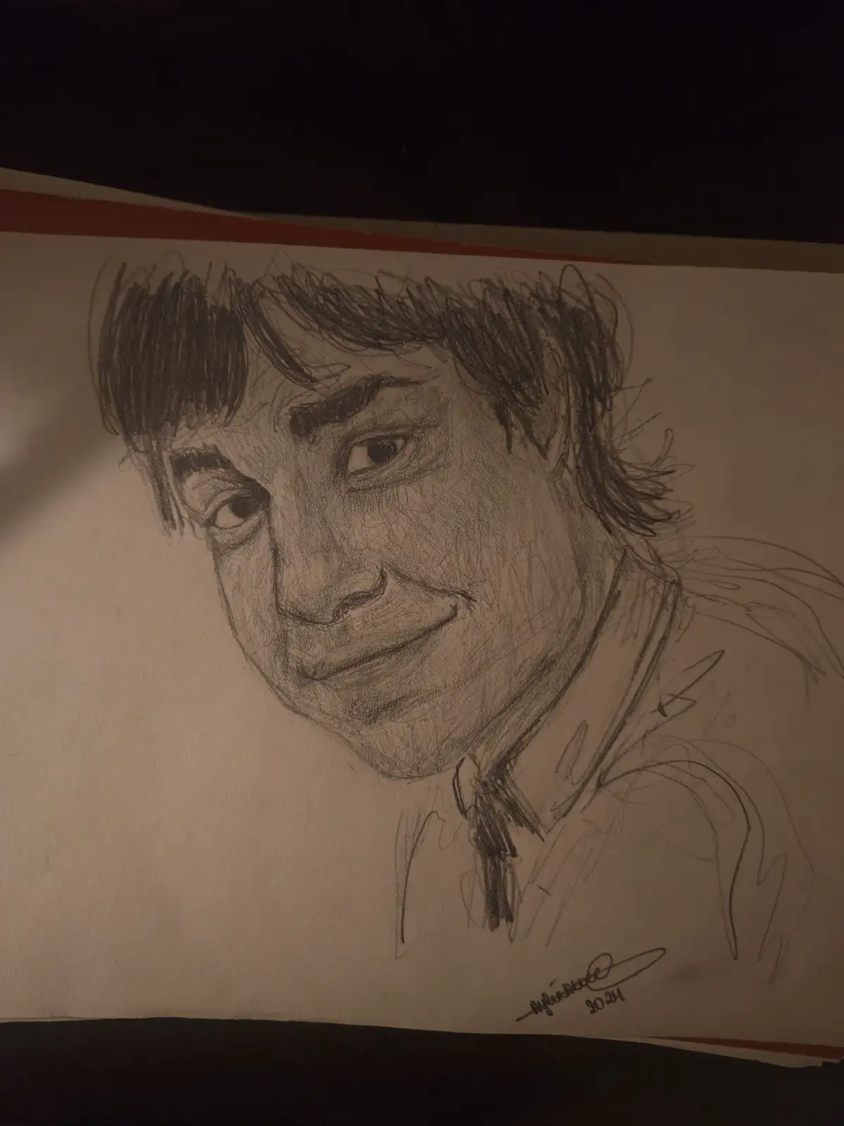 A hand-drawn pencil sketch on paper depicts a person with messy hair, a slight smile, and a tilted head, wearing a collared…