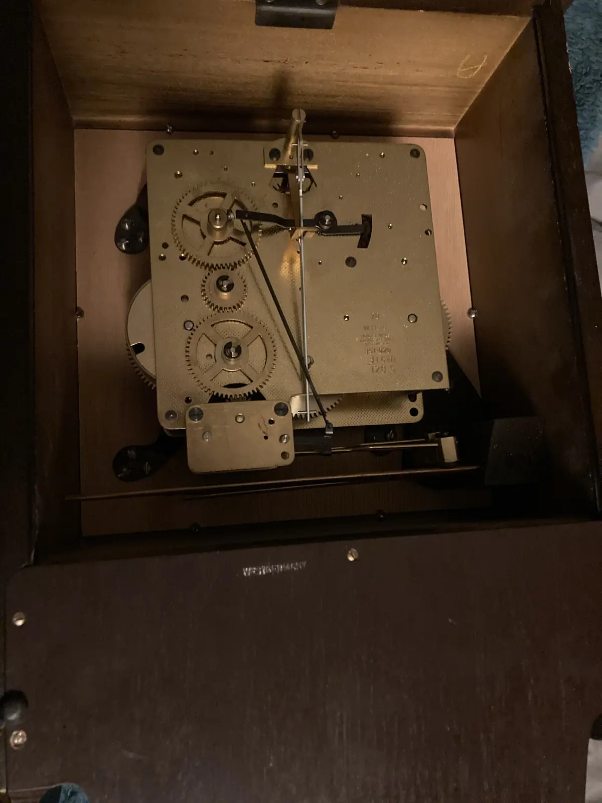 A close-up photo shows the internal mechanical movement of a wooden clock, featuring brass gears, a pendulum rod, and a…