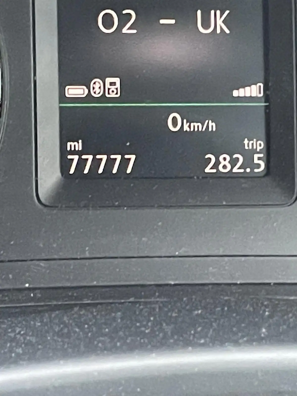 A close-up of a car's digital dashboard showing '02 - UK' at the top, a speed of '0 km/h', and a mileage reading of 'mi…