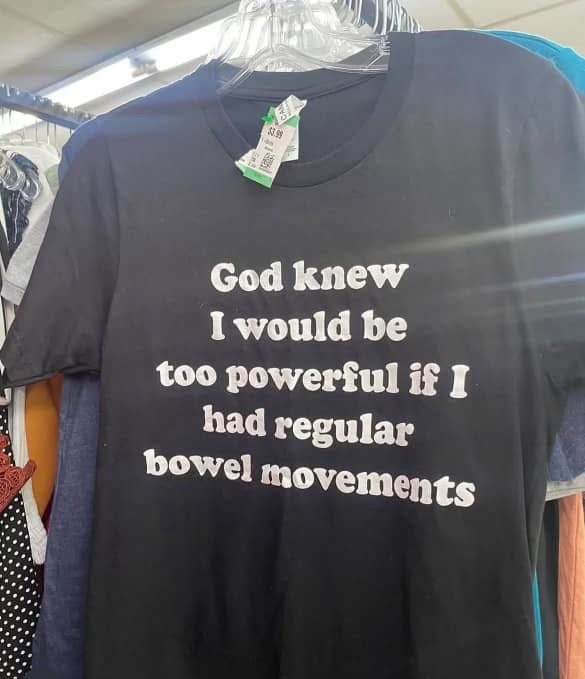 A black t-shirt hangs on a plastic hanger in a clothing store, displaying white text that reads 'God knew I would be too…