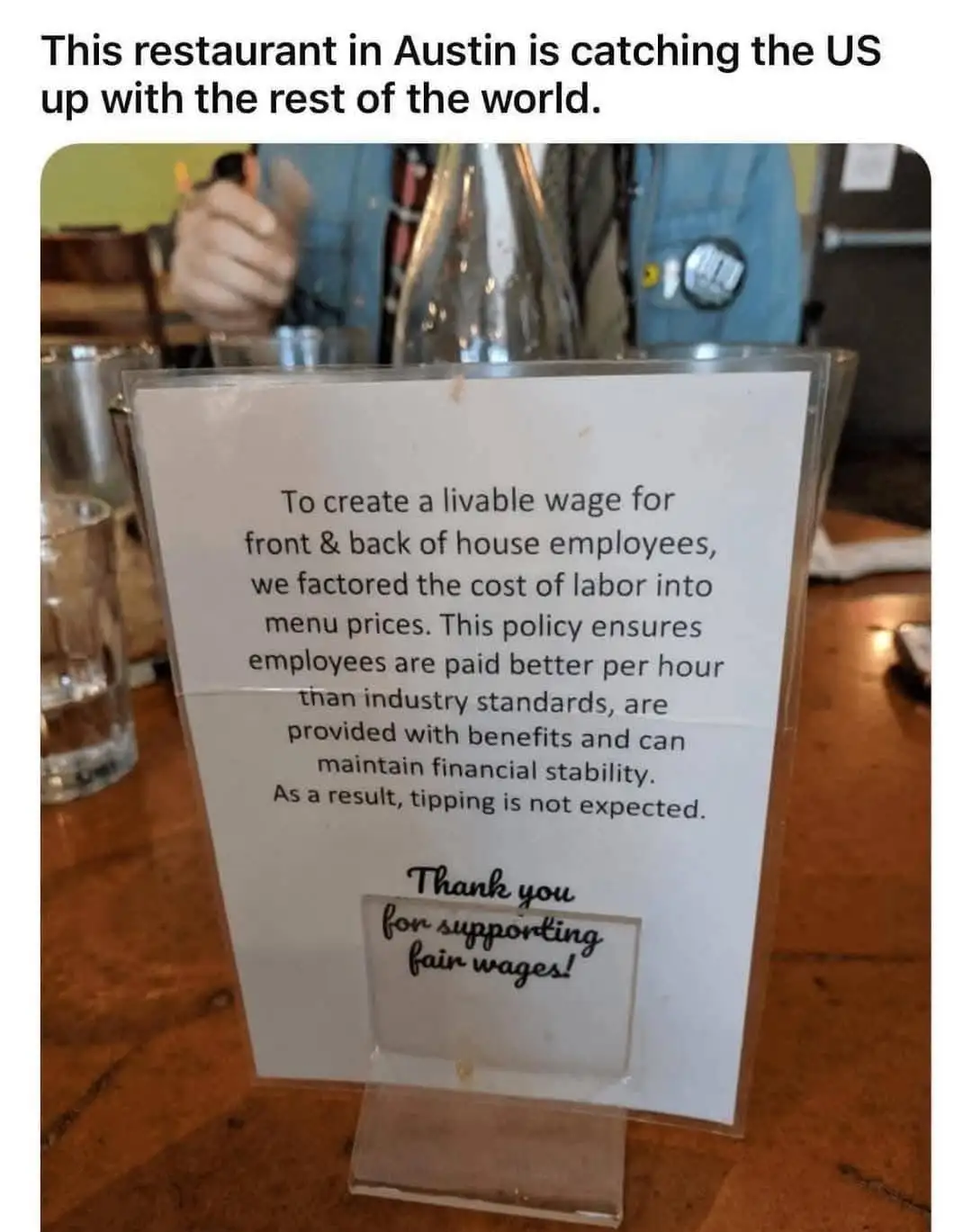 A sign on a restaurant table explains that labor costs are factored into menu prices to ensure employees earn a livable…