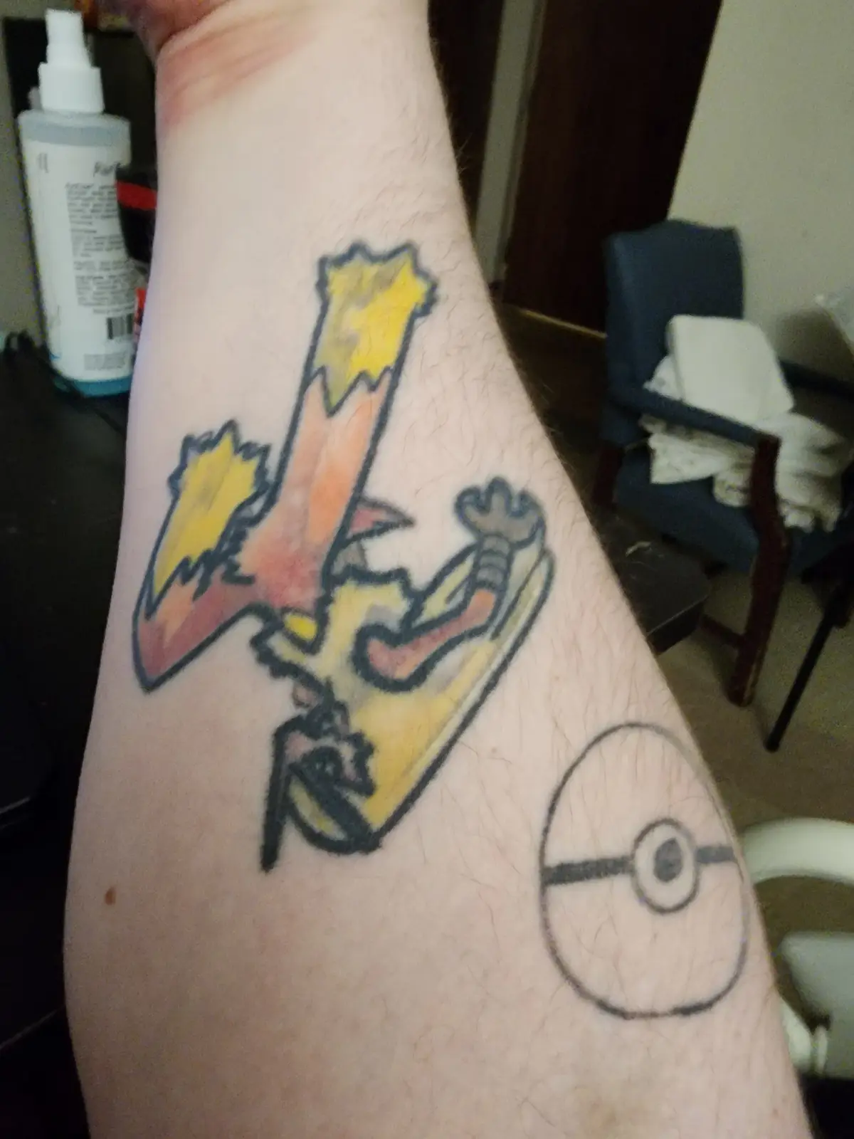 A person's forearm displays two tattoos: a colorful, cartoon-style depiction of the Pokémon Charizard in mid-flight with…