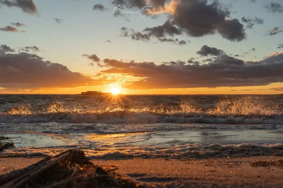 A serene sunset over the ocean with waves crashing onto a sandy beach, the sun low on the horizon casting golden light…