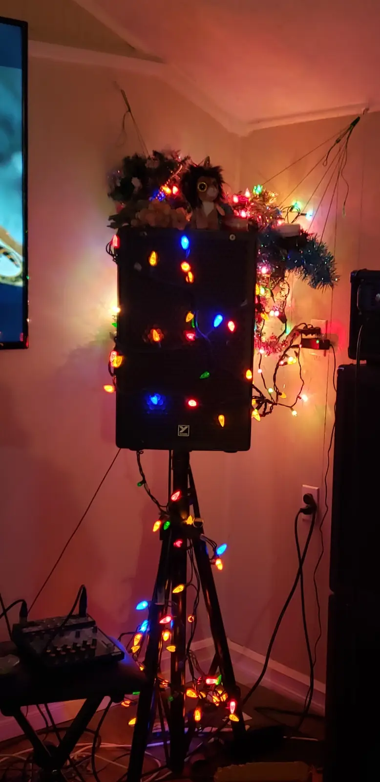 a large black speaker on a stand is heavily decorated with multicolored christmas lights, tinsel, and a stuffed animal on…