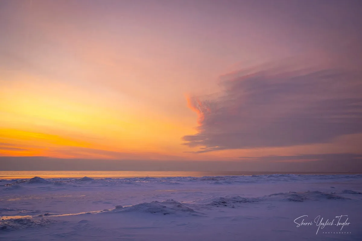 A serene winter sunset over a frozen, snow-covered landscape with vibrant orange and purple skies. The overlaid text reads…