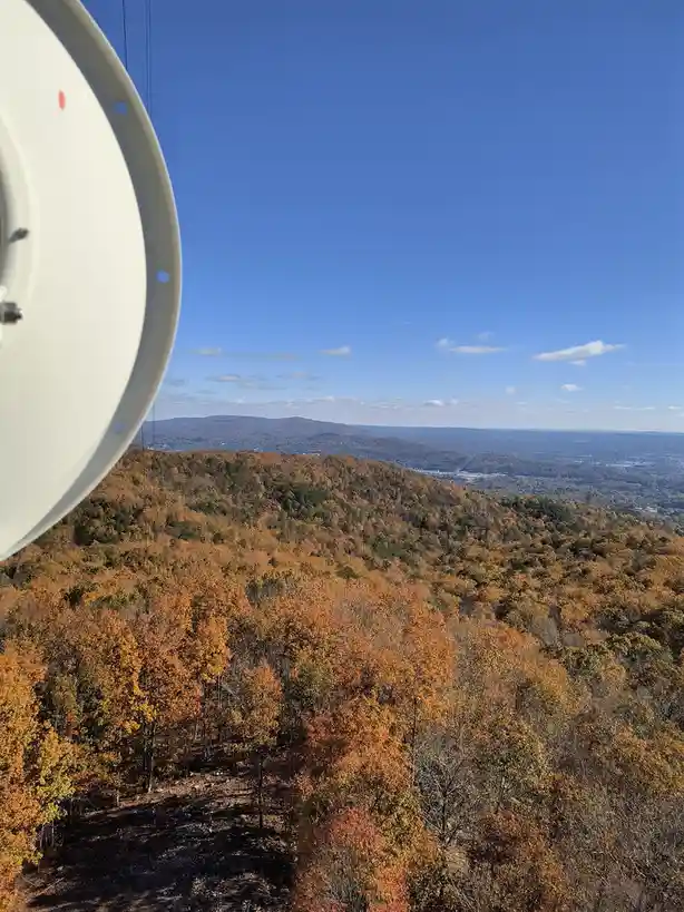 A scenic autumn view from a high vantage point shows rolling hills covered in orange and brown foliage under a clear blue…