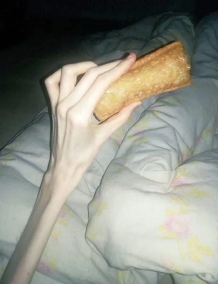 A person's slender hand holds a golden-brown, rectangular fried food item, likely an egg roll or spring roll, over a…
