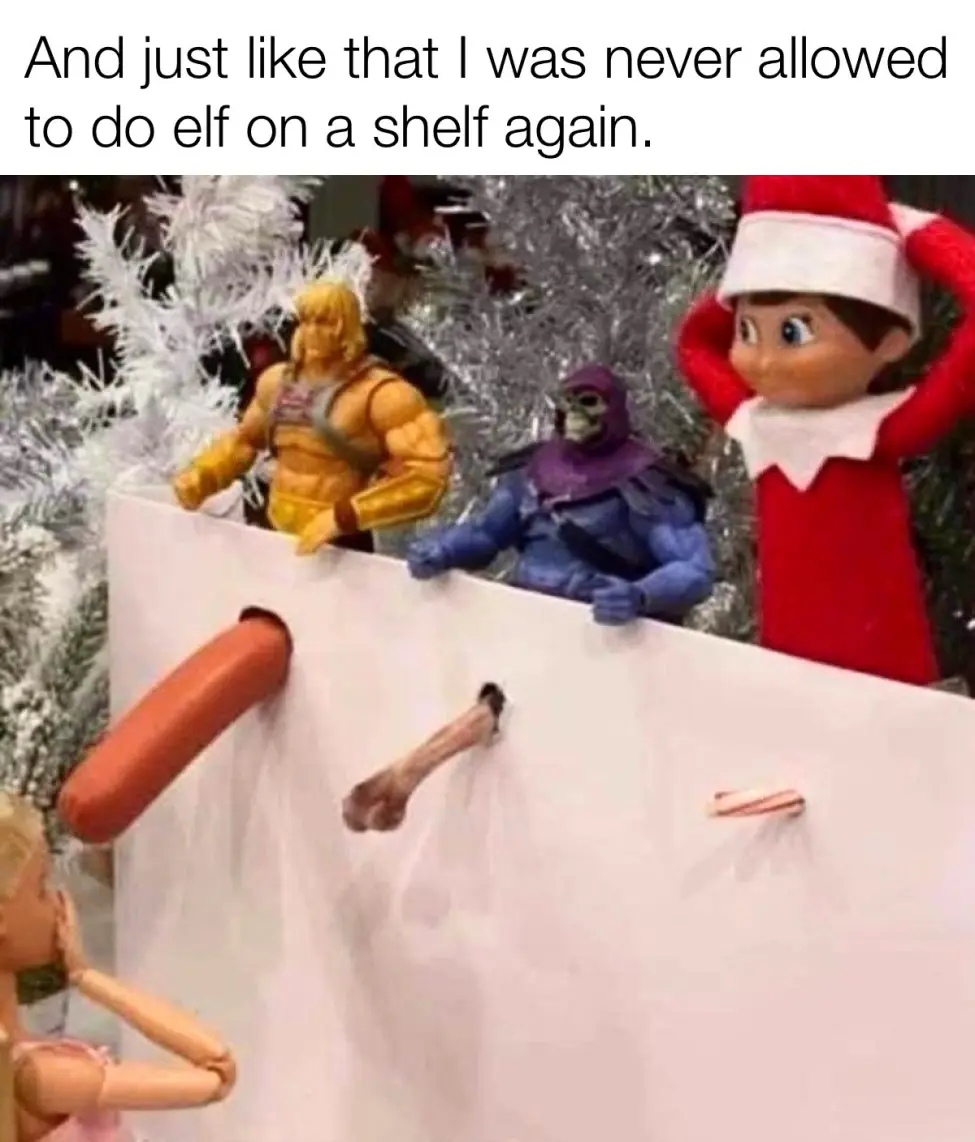 A toy elf in a red suit with a white hat stands behind a white cardboard barrier, looking shocked with hands on head. Behind…
