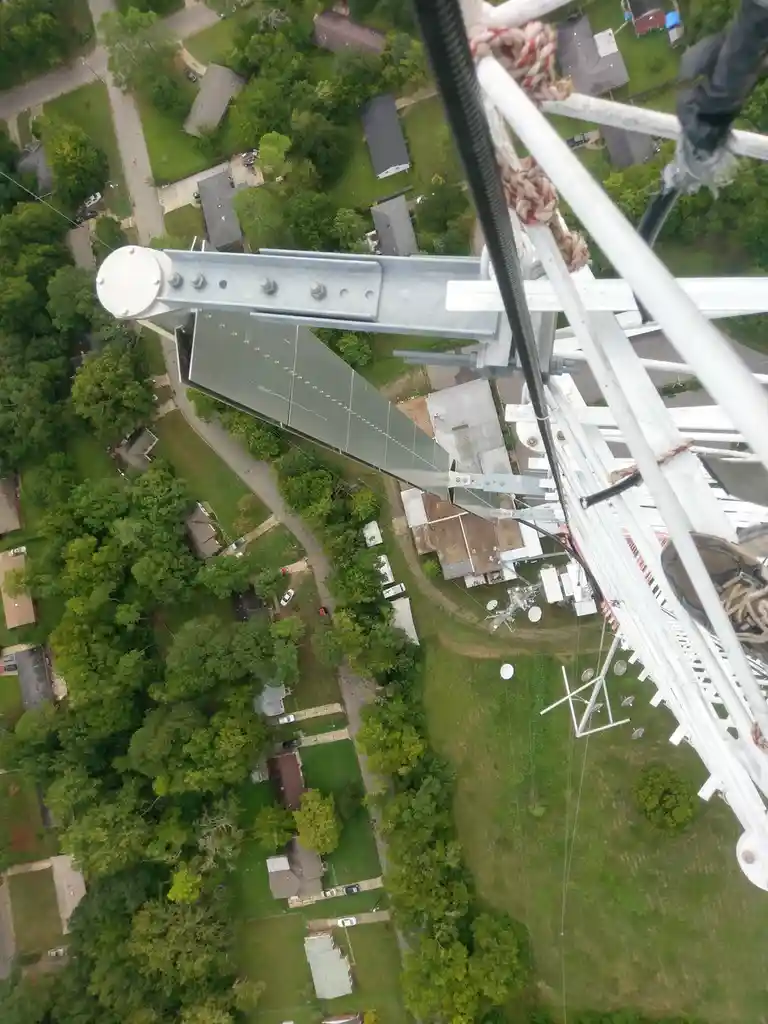 An aerial view from the top of a tall metal communications tower looking down at a suburban neighborhood with houses, trees…