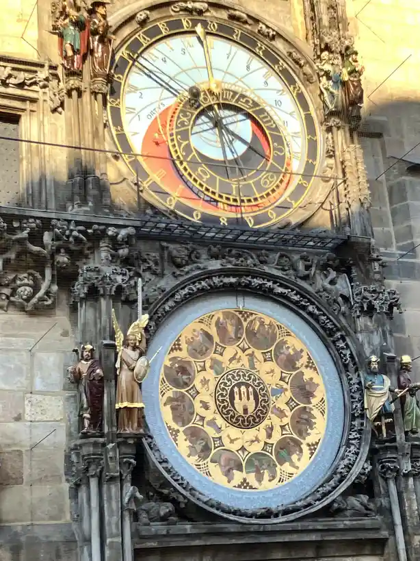The image shows the ornate Prague Astronomical Clock, featuring a large upper clock face with zodiac signs and Roman…