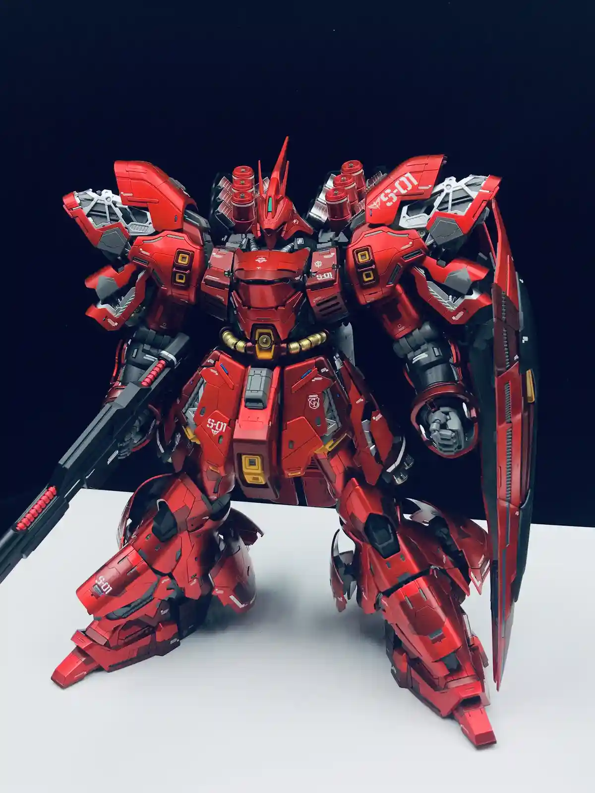 A highly detailed, red and black custom-built mecha model, resembling a Gundam, stands in a dynamic pose on a white surface…