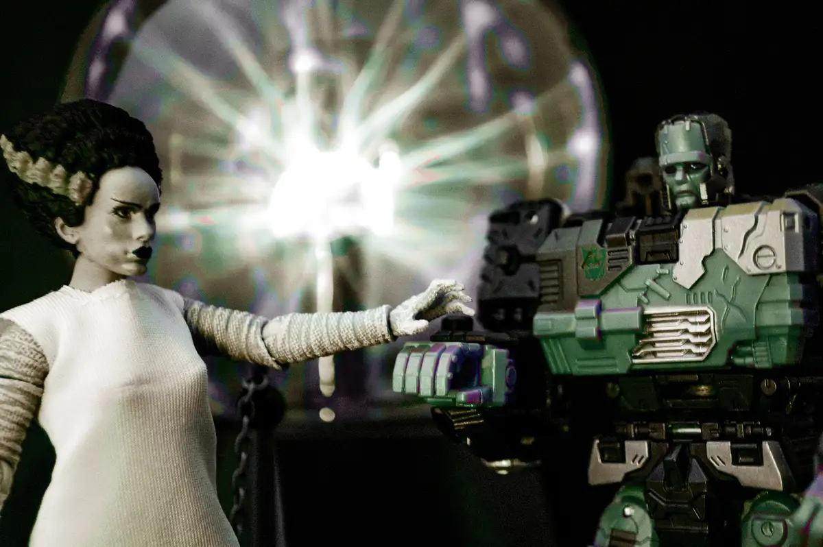 A figurine of a woman with dark hair and a white dress extends her hand toward a green and silver robot. Between them, a…