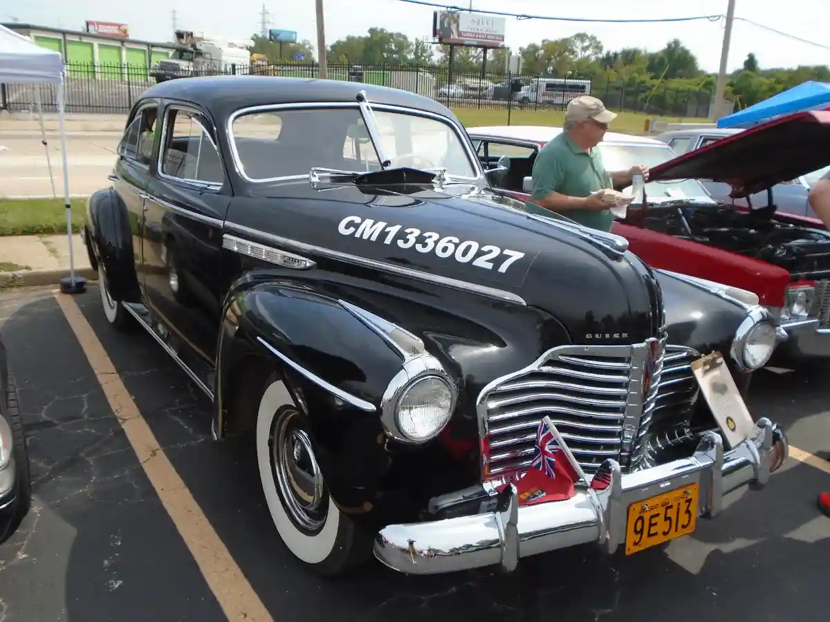 A black 1940s Buick classic car with white wall tires and chrome trim is parked at a car show, featuring a Canadian flag and…