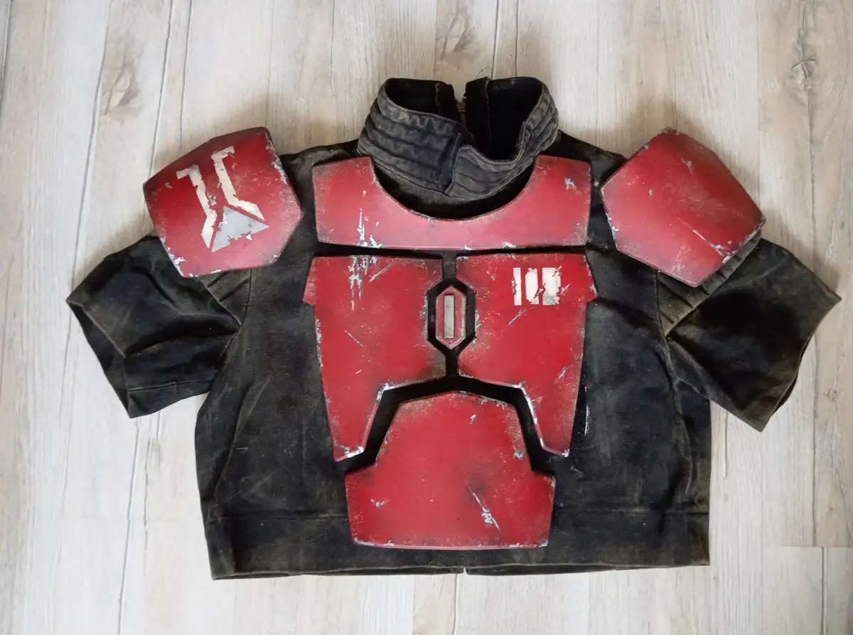 A child-sized black jacket with red, weathered armor plating over the chest and shoulders, featuring white markings…