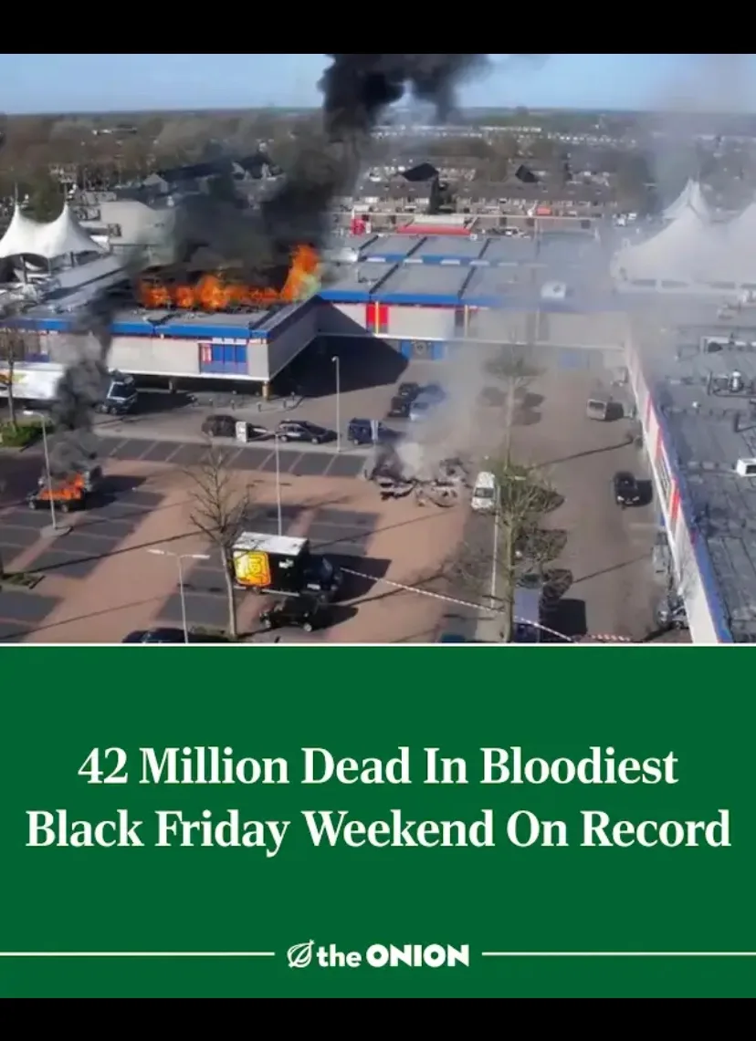 An aerial view shows a large commercial building on fire with thick black smoke rising, surrounded by a parking lot with…