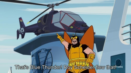 An animated character in a yellow and orange costume with a horned helmet stands on a ship's deck, pointing upward at a dark…