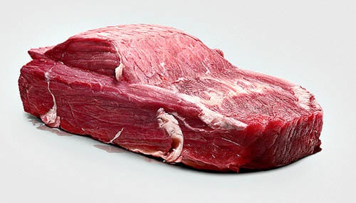a raw, red piece of meat is shaped to resemble a car, with visible muscle fibers and fat forming the body, hood, and wheels…