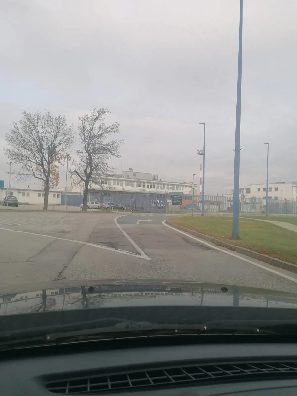A photo taken from inside a car looking out at a large, fenced industrial or institutional complex with multiple buildings…