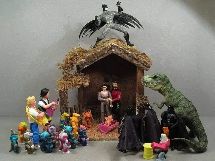 A diorama depicts a nativity scene with Star Trek characters in the manger holding a baby, Batman perched atop the roof, a…