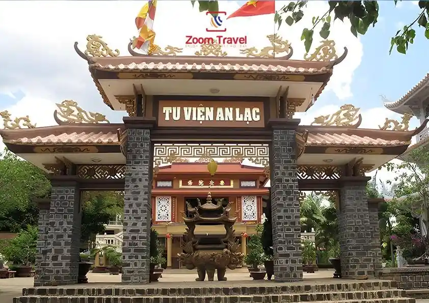 A photograph of a traditional Vietnamese temple gate with ornate golden roof details and stone pillars, featuring the sign…