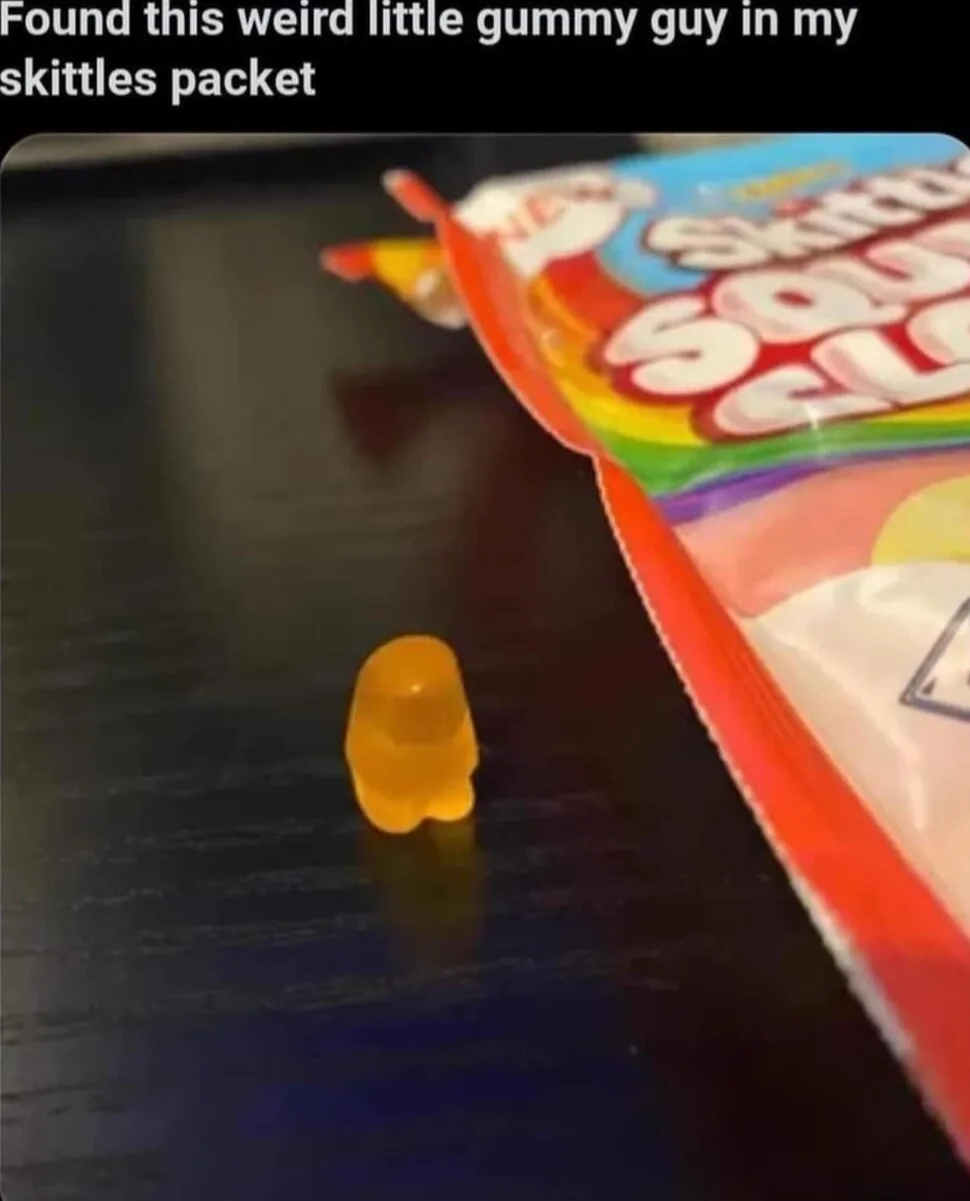 A close-up photo shows a small, yellow, gummy bear-shaped candy standing upright on a dark wooden surface next to an open…