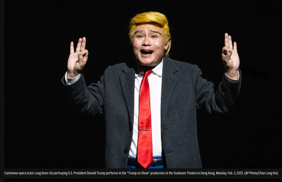 A man in a dark suit, white shirt, and red tie, wearing a bright yellow wig, stands against a black background with both…