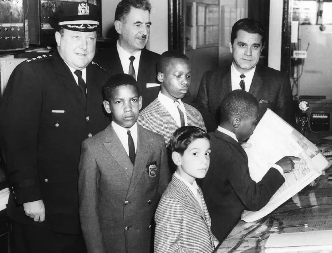 a black-and-white photo of six men and boys in suits, including a police officer and several young boys, standing in what…