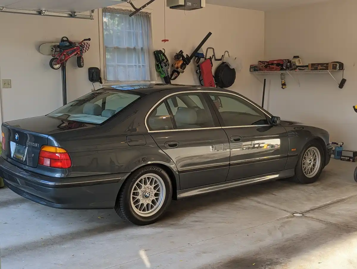 A dark gray BMW 528i sedan is parked in a clean, well-lit garage. The car has silver multi-spoke wheels and light-colored…