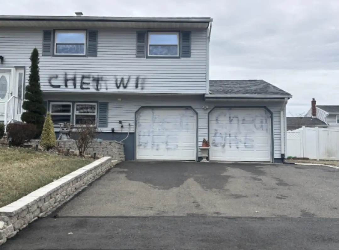 A residential house with graffiti on its exterior walls and garage doors. The words 'CHEAT WIFE' are spray-painted in large…