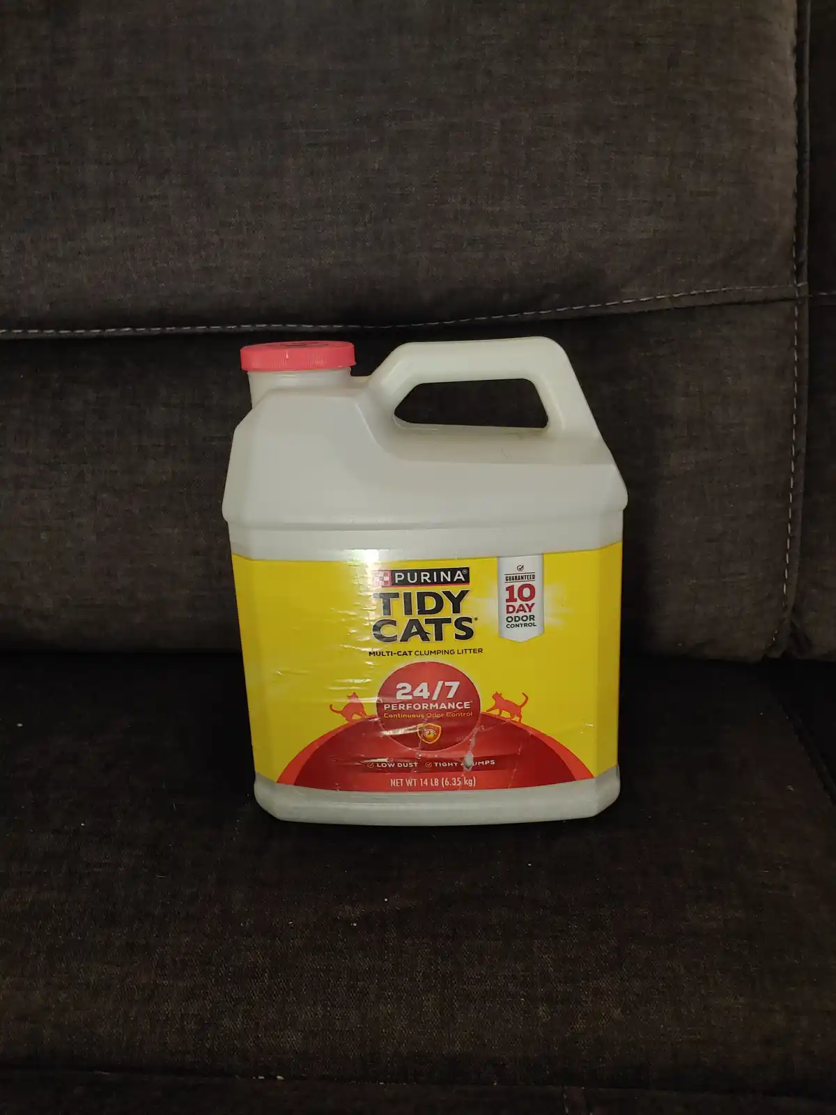 A large white plastic jug of Purina Tidy Cats multi-cat clumping litter, with a yellow and red label, sits on a dark brown…