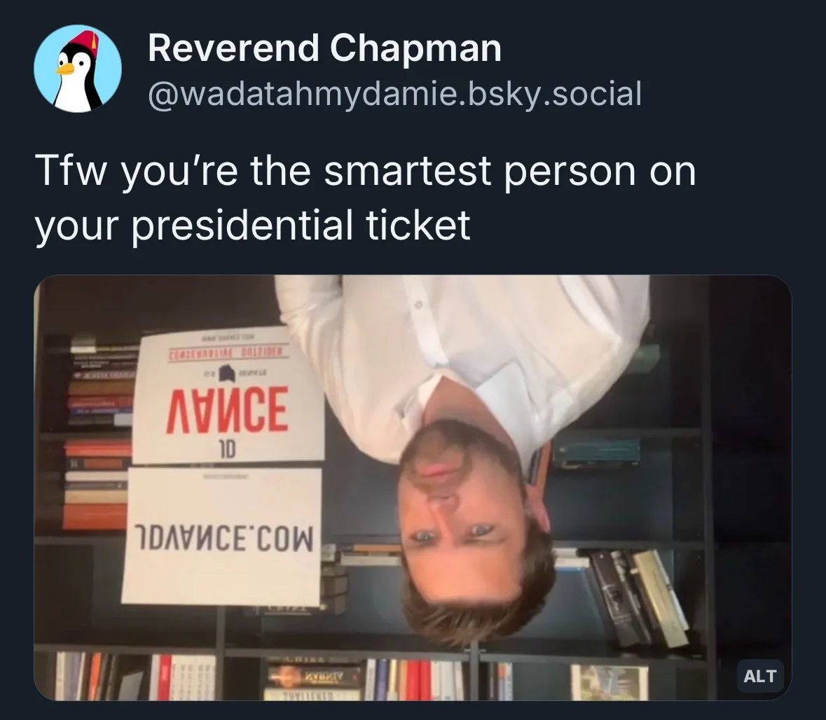 A man in a white shirt is shown upside down in front of a bookshelf, looking upward with a confused or overwhelmed…