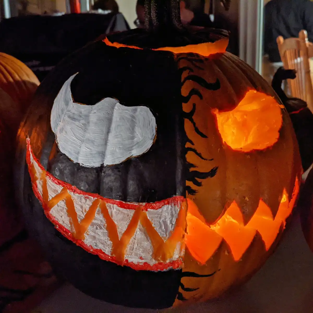 A carved Halloween pumpkin with one side painted black and white to resemble a tiger's face, featuring a white eye, black…