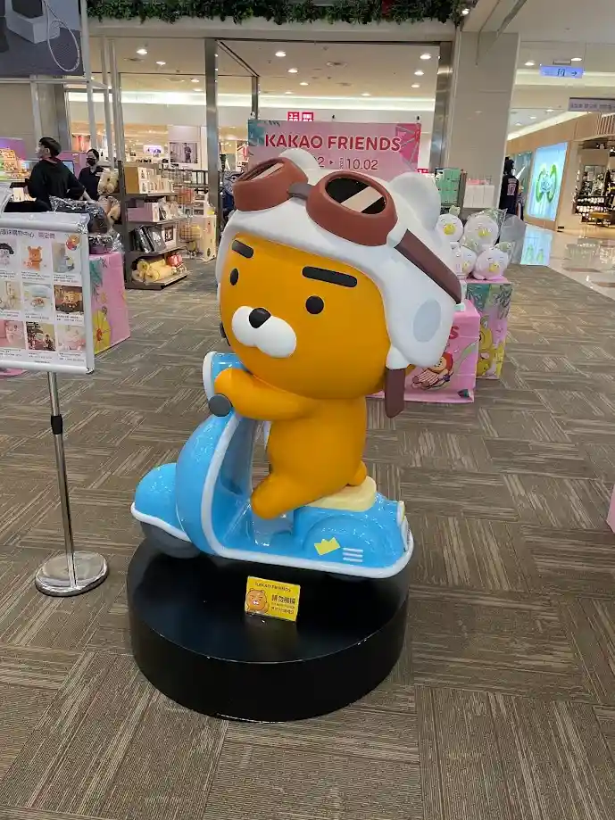 A large, yellow cartoon bear statue wearing aviator goggles and a white helmet, sitting on a blue scooter display in a…